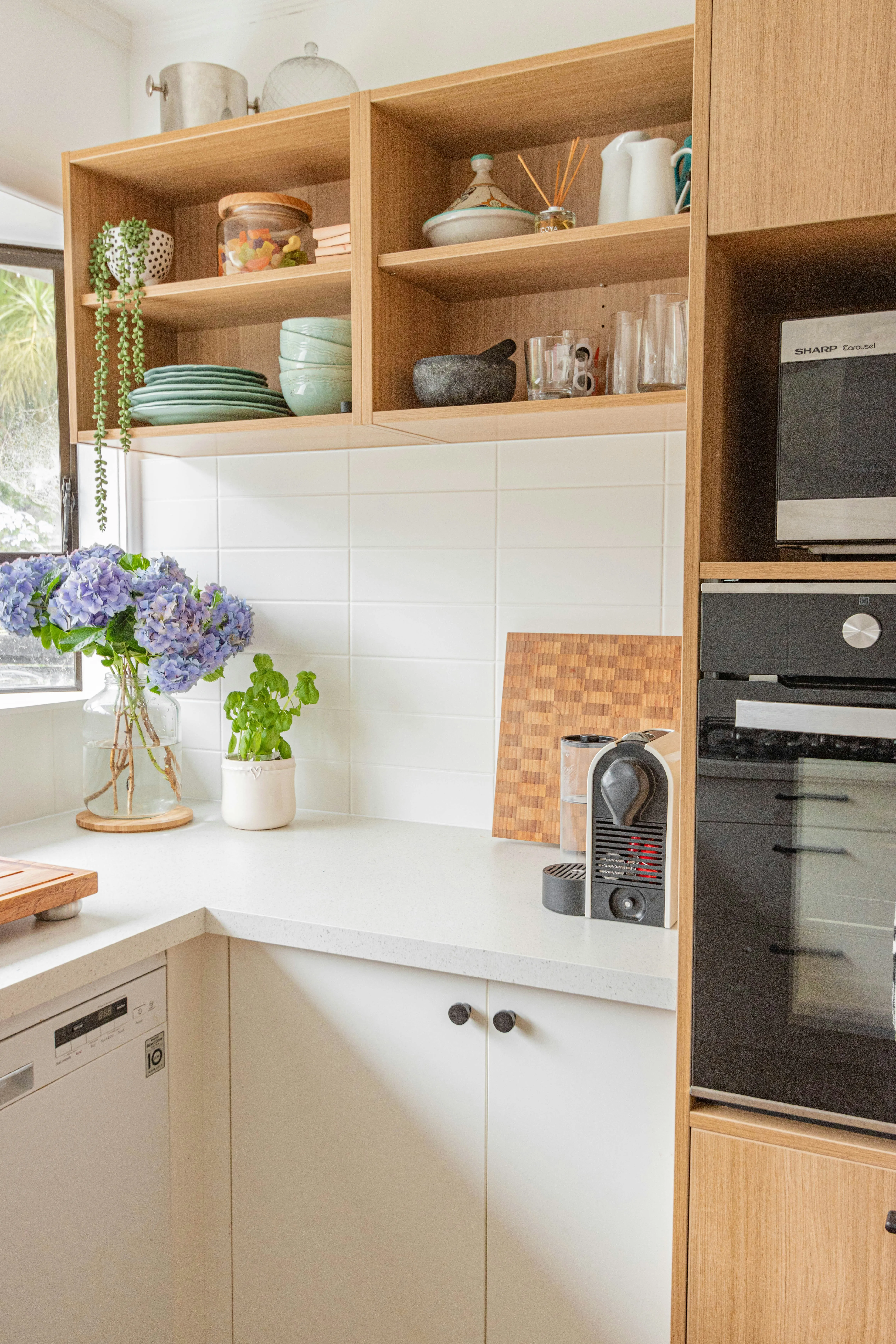 A bright, organized kitchen with wooden shelves and fresh flowers
